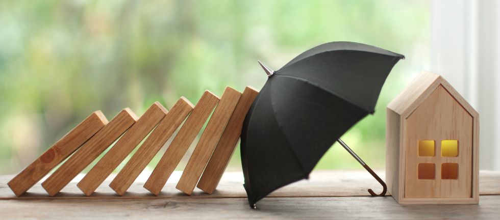 Image illustrating home insurance with an umbrella protecting the house from falling bricks